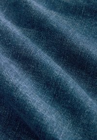Denim-kangas, jossa on syvän tummansininen väri, pehmeä rakenne, näkyvät kudontakuviot ja hienovaraiset korostukset valonheijastuksista.