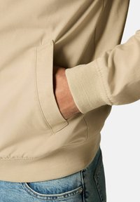 Sweatshirt beige avec une finition texturée, des poignets côtelés et une poche latérale. Conçu avec une coupe décontractée et des détails de coutures subtils.