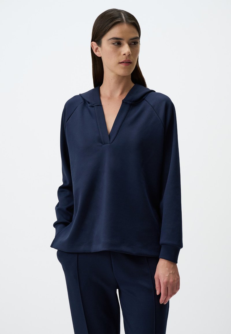 Felpa blu navy con scollatura a V e cappuccio. Tessuto morbido, maniche lunghe e vestibilità rilassata. Abbinata a pantaloni blu navy coordinati.