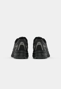 Baskets de sport noires avec une tige en mesh, des accents texturés et une semelle rembourrée, dotées d'un design épuré et ergonomique pour le soutien.