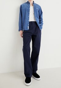 Chemise bleu clair à boutons, sous-vêtement blanc, pantalon bleu marine foncé et baskets noires avec semelles blanches. Textures lisses et coupe décontractée.