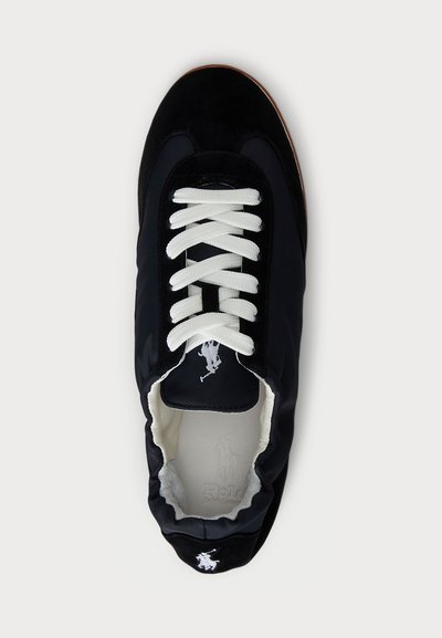 Scarpa sportiva nera realizzata con materiali in tessuto e camoscio, caratterizzata da lacci bianchi, una punta arrotondata e un logo sul linguetta.