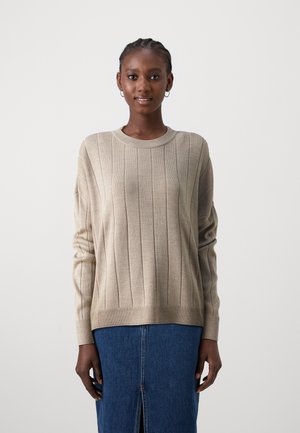 Maglione beige lavorato a maglia con texture a coste verticali, collo rotondo e maniche lunghe. Abbinato a una gonna di jeans con spacco frontale.