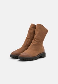 Botas de tobillo marrones hechas de cuero suave con un diseño arrugado, punta redonda y suelas de goma gruesas. Acabado texturizado con acentos mínimos.