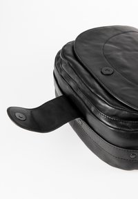 Mustalainen nahkakassi pyöreällä muotoilulla, jossa on napsautuslukitus ja teksturoitu pinta, joka esittelee tyylikästä ja sileää ilmettä.