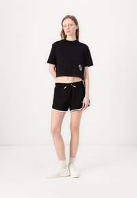Svart kort t-skjorte med korte ermer, med en hvit logo, parret med svarte shorts med hvit kant og elastisk linning.