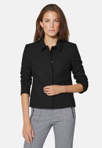 Zwarte jas met een kraag, twee voorzakken en knoopsluiting. Lange mouwen met ribgebreide manchetten, gecombineerd met geruite broek.