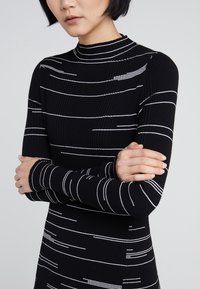 Top a maniche lunghe nero a coste con strisce orizzontali bianche, collo alto, design aderente e tessuto testurizzato, che mette in mostra dettagli senza cuciture.