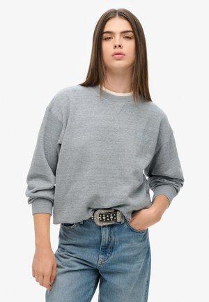 Felpa grigia in morbido tessuto con polsi e scollatura a costine. Abbinata a jeans in denim blu e una cintura nera con dettagli in argento.