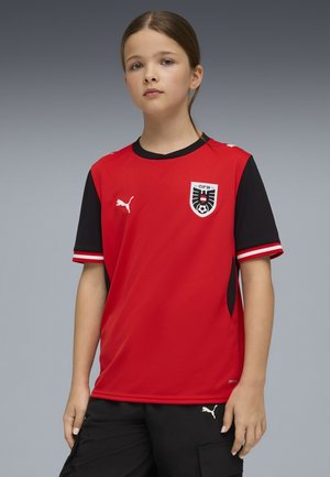 Piros-fekete rövid ujjú focimez kerek nyakkivágással, mellrészen logóval és texturált anyaggal. Fehér csíkokkal díszítve.