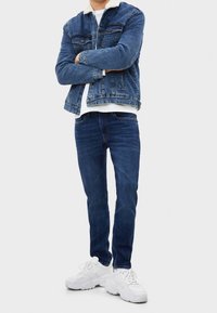 Jeansjacka med fårskinnskrage, blå jeans och vita tjocka sneakers. Viktiga egenskaper inkluderar en knappstängd framkant och klassisk denimstruktur.