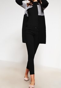 Schwarz-grauer Farbblock-Cardigan mit langen Ärmeln, geschichtetem Design, kombiniert mit schwarzen Skinny Jeans und flachen Schuhen mit Blumenmuster.