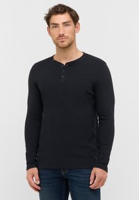 Schwarz langärmliges Henley-Shirt mit einer Drei-Knopf-Leiste, gerippten Bündchen und strukturiertem Stoff. Getragen mit blauen Jeans.