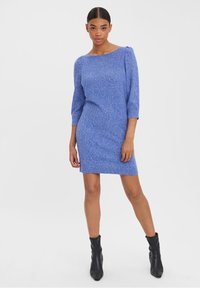 Robe tricotée bleue avec des manches trois quarts, ourlet côtelé et tissu texturé. Portée avec des bottines noires à cheville.