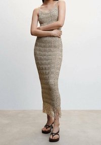 Robe beige en maille avec une silhouette ajustée, un décolleté carré et un ourlet à franges. Associée à des sandales à plateforme marron à brides.