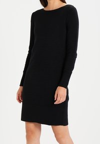 Svart stickad klänning med lång ärm, med ribbad textur, rund halsringning och en något figurnära passform.