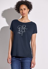 Camiseta de manga corta azul marino de algodón, con un diseño gráfico plateado brillante que incluye texto. La tela tiene una textura suave.