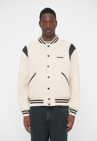 Crème varsity jack met zwarte leren schouderaccenten, geribbelde manchetten en banded hem. Kenmerkt zich door drukknoopsluiting en een subtiele logo op de borst.