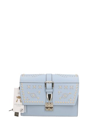 Borsa in pelle blu con chiusura a pattina, caratterizzata da borchie argentate e una fibbia metallica. Include un'etichetta che descrive l'artigianato fatto a mano.