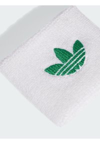 Witte katoen polsband met een gestructureerd oppervlak, voorzien van een groen geborduurd logo met drie bladeren en drie parallelle lijnen.