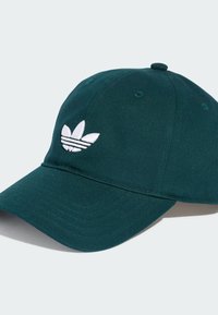 Casquette en coton vert foncé avec une visière courbée, ornée d'un logo trois bandes brodé en blanc et d'un bouton sur le sommet. Tissu texturé.