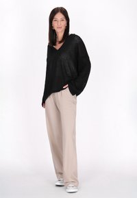 Pulover negru oversize cu un decolteu în V, combinat cu pantaloni bej cu talie înaltă și adidași albi. Textură moale și croială lejeră.
