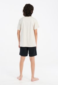 Camiseta de algodón beige con mangas cortas y cuello redondo, combinada con pantalones cortos negros. Los pantalones cortos tienen un diseño simple y son de longitud hasta la rodilla.
