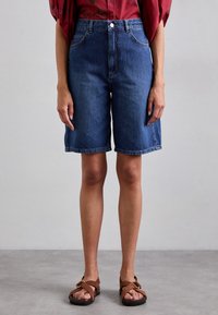 Farkkushortsit korkealla vyötäröllä, tummansininen väri ja suora lahje. Viimeistelty viiden taskun tyylillä ja nappikiinnityksellä.