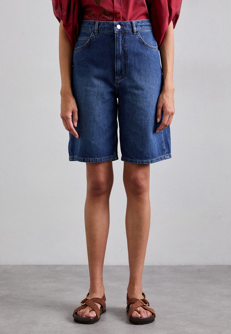 Denim šorti ar augstu jostu, tumši zila krāsa un taisna piegriezuma kāja. Pabeigti ar piecu kabatu dizainu un pogu aizdari.