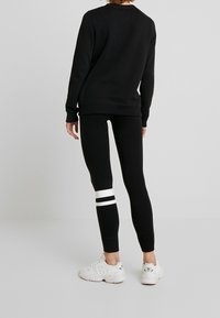 Černá mikina s pletenými manžetami, spárovaná s černými legínami se bílým pruhem přes koleno. Outfit doplňují bílé tenisky.