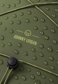Olívovo zelená vodeodolná látka s vystúpenými bodkami a kvapkami vody. Logo "JOHNNY URBAN" vytlačené nažlto spolu s čiernym nastavovacím prackou.