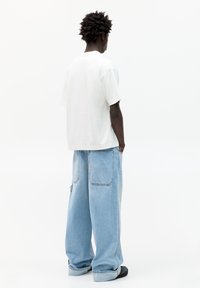 Tricou alb din bumbac cu maneci scurte, asortat cu blugi din denim decolorat, cu tăietură largă, având două buzunare la spate.