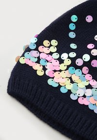 marineblå strikket lue pyntet med flerfargede paljetter i rosa, blått og gult, med ribbestrikket kant og glatt tekstur.
