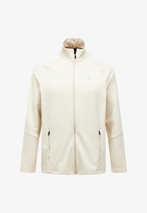 Veste zippée beige clair en tissu doux, avec un col haut, deux poches latérales zippées et un discret logo sur la poitrine.