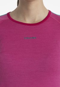 Fuchsia långärmad topp med rund hals, gjord av ull, med en smal passform. "Icebreaker"-logotyp i teal nära halsringningen.