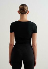 T-shirt nera aderente con maniche corte e scollatura rotonda, abbinata a leggings neri a vita alta. Texture liscia, branding minimale.
