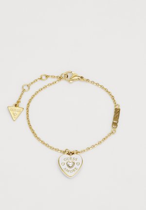 Brăţară din aur cu un pandantiv în formă de inimă inscripționat cu "GUESS AMORE" și un accent din cristal, plus un pandantiv triunghiular gravat cu "GUESS."