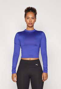 Fitted, long-sleeve crop top in deep blue, smooth texture, round neckline, paired with high-waisted black leggings featuring a logo.