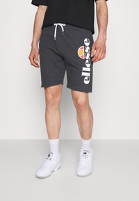 Shorts en coton gris avec cordon de serrage blanc et grand logo "ellesse" blanc. Porté avec des baskets blanches et des chaussettes courtes. Conception décontractée et ajustement sportif.