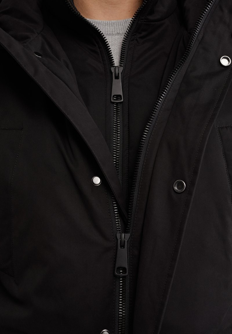 Schwarz isolierte Jacke mit vollem Reißverschluss, Druckknöpfen und einer weichen Stoffstruktur. Das Design beinhaltet eine Kapuze und seitliche Taschen.