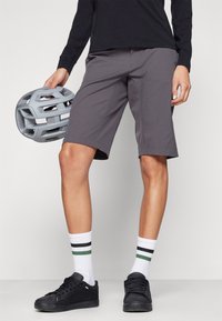 Grå sykkelshorts laget av lett materiale, med avslappet passform og sidelommer, kombinert med svarte sko og stripete sokker.