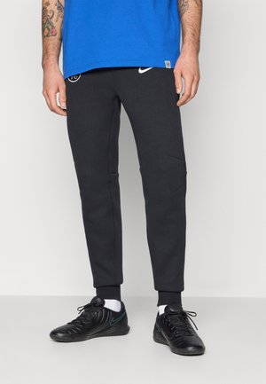 Black sweatpants with ribbed cuffs, featuring side pockets and a logo on the left thigh, complemented by black athletic shoes with a teal accent.