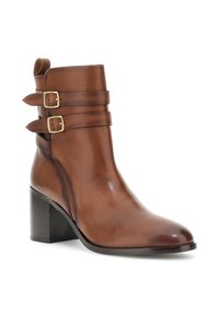 Hnědá kožená kotníková bota se zaoblenou špičkou, robustním černým podpatkem a dvěma zlatými přezkami kolem kotníku pro ozdobu. Hladký povrch.