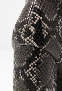 Primo piano di pelle con stampa rettile nera e grigia, caratterizzata da una texture a scaglie esagonali e cuciture visibili.