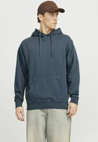 Sudadera con capucha de color azul marino, hecha de una mezcla de algodón, que presenta un bolsillo canguro, cordones y puños y dobladillo acanalados. Se lleva con jeans claros.