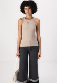Beige ribbet t-skjorte med rund hals og liten logo detalj; kombinert med vidbenede mørke jeans med oppbrettede kanter og en hvit håndveske.