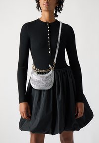 Ribota melna blūze ar sudraba pogām, kopā ar apjomīgu melnu svārku. Iezīmēta maza sudraba metāla crossbody soma ar ķēdes siksnu.