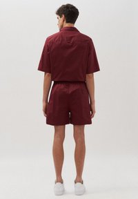 Camicetta bordeaux a maniche corte e pantaloni corti abbinati realizzati in tessuto leggero. Vita elasticizzata, vestibilità casual, con dettaglio della tasca posteriore. Sneakers bianche.