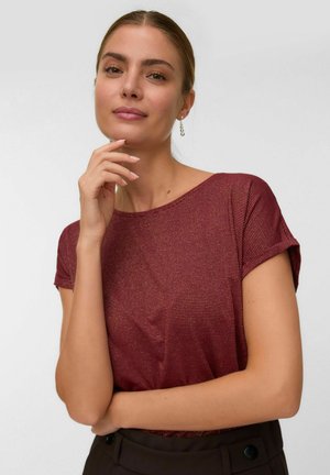 Woman with light brown hair tied back wearing a maroon short-sleeve top and dangling silver earrings, posing with hand near chin.