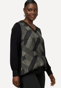 Zwarte en geprinte blouse met V-hals, met gestructureerde grijze en gouden geometrische ontwerpen aan de voorkant en zwarte mouwen met glinsterende accenten.
